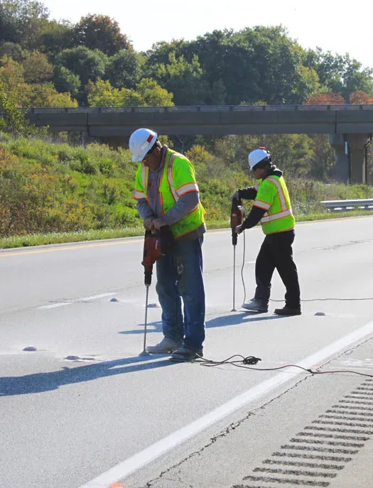 Two technicians drilling holes in roadway