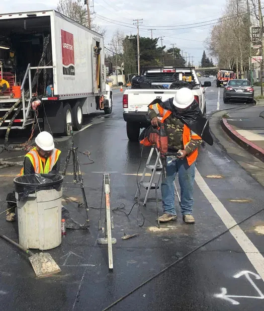 URETEK technicians drill holes on wet pavement