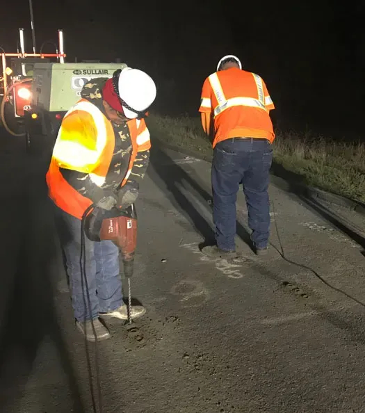 Two URETEK technicians drill holes in pavement at night