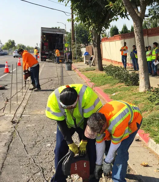 Two technicians in safety equipment work with concrete over a surface with another in the background