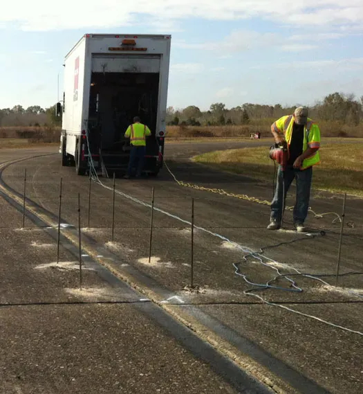 URETEK technicians drilling hole in highway as crewmember accesses rear of semi-truck